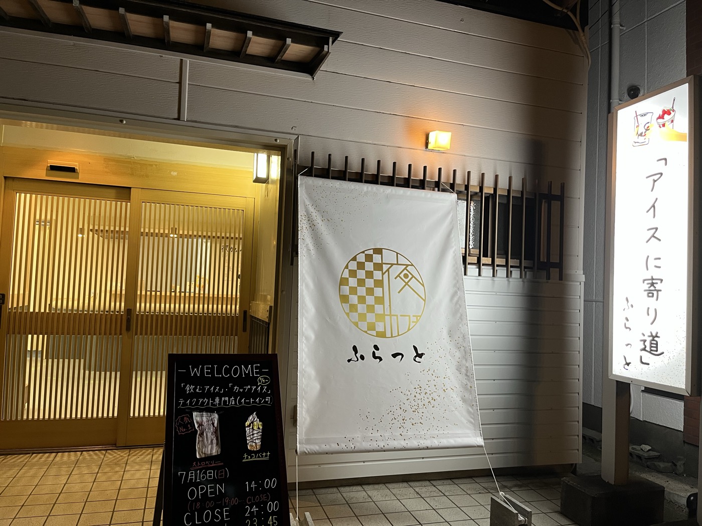 夜のふらっとの入口。金色のロゴの暖簾と「アイスに寄り道」の看板が出ている